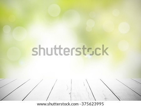 White old wood floor with blurred green leaves background. Wooden planks stage and blur leaf with flare sunlight. Abstract medical backdrop. Focus to table top in the foreground. Sun rays blur bokeh.