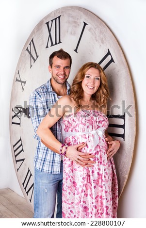 Happy Pregnant Couple on white background with giant clock