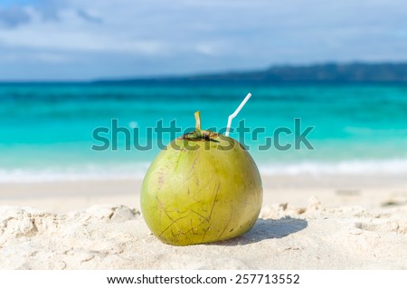 Tropical green coconut cocktail with drinking straw on a sand against background of turquoise sea lagoon at exotic white sandy beach on paradise Boracay island, Philippines.