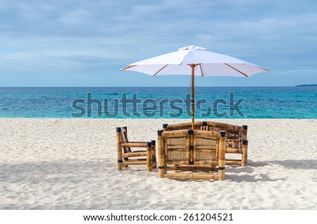 Tropical beach resort view with turquoise sea, lonely beach table with chairs from bamboo and umbrella on exotic white sandy Puka beach on Boracay, Philippines