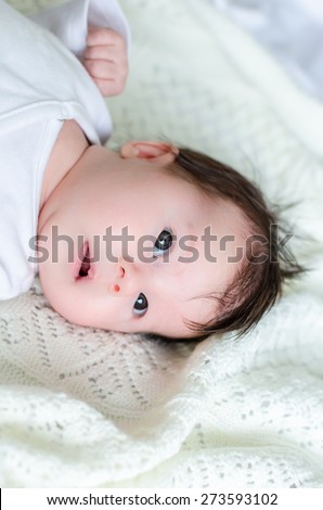 Sweet little newborn baby daughter looking with big beautiful hazel brown eyes, curious glance and open mouth on white woolen blanket at home