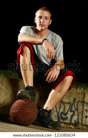 Young basketball player sitting down for a break, foot on the ball and looking at camera