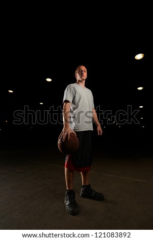 Basketball player standing and looking at camera with ball in hand at night