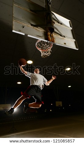 Basket and basektball player jumping with ball and aiming at basket at night