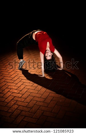 Girl doing a breakdance move at night on brick floor, wearing a red t-shirt