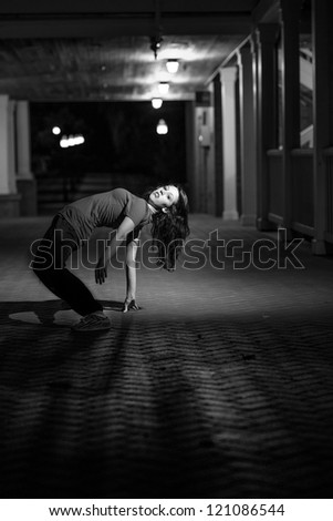 Girl doing a breakdance move at night on brick floor. B&W image