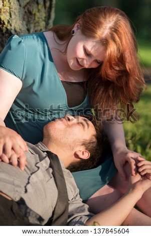 Happy couple talking and relaxing outdoors, with man lying with his head in the woman's lap