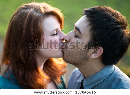 Amorous attractive young couple kissing outdoors backlit by the evening sun, head and shoulders portrait