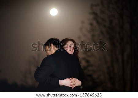 Loving young couple hugging each other in a close embrace on a misty evening under the moon