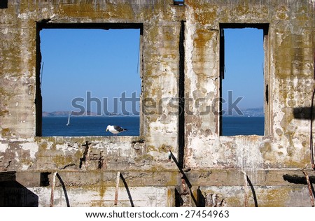 An old building outline with a bird standing in a window frame with blue ocean and sky in background.