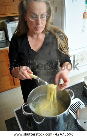 woman cooking spaghetti noddles boiling in large pan of hot steaming water.