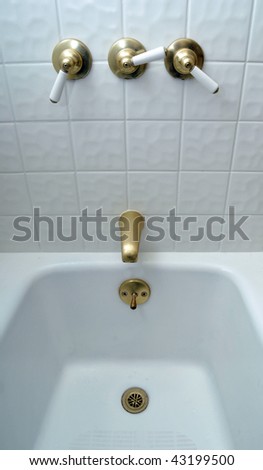 New golden bathtub valves on white tile