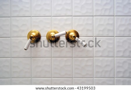 Three golden shower valve handles ona  big white empty tile shower room
