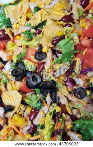 Delicious taco salad closeup. Contains black olives, green lettuce, red tomatoes, yellow cheddar cheese, purple kidney beans, white tender chicken, yellow corn and orange carrot shavings.