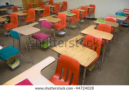 An empty class room with no students sitting in the desks. There are some notebooks laying around the room (none contain any logos.)