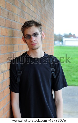 A healthy tall white male Caucasian student stands in front of a brick wall with his backpack on