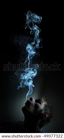 Young adult white Caucasian man smokes in a dark room. The smoke is glowing against the black background