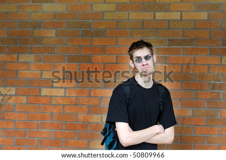 A healthy tall white male Caucasian student stands in front of a brick wall with his arms crossed with confidence. Background has lots of room for your text.