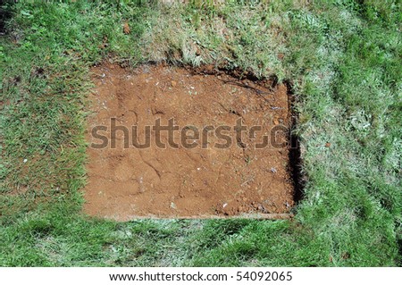 A flat dirt patch is surrounded by green grass. This is really a filled hole with dirt.