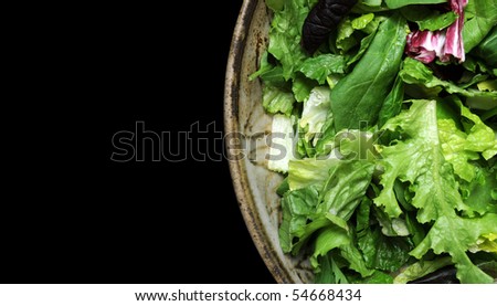 A variety of green lettuce tossed in a salad bowl isolated on a black background