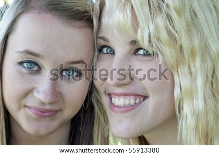 Closeup photograph of two pretty blond girl friends smiling at the camera.