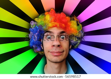 A silly crazy man wearing a clown wig with rainbow colors behind him