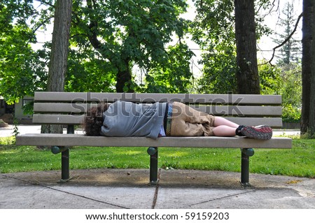 A homeless person takes a nap on a bench in a public park.