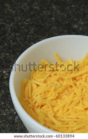 An aerial view of a white bowl containing yellow cheddar cheese on a black counter top