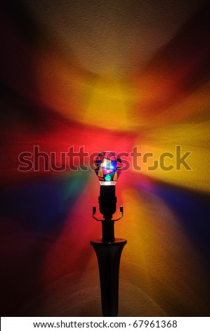A colorful lightbulb with painted rainbow colors projecting onto the wall behind it with copyspace with room for your text