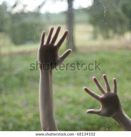 Hand touching a glass window with raindrops over a defocused nature background