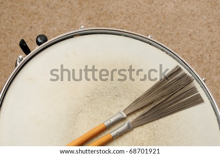 A direct overhead above view of a snare drum on a stand with drum brushes
