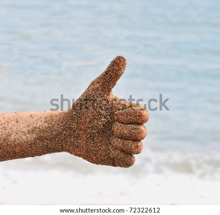 Beach fun with a wet hand with sand on it giving a thumbs up. Ocean beach waves in the background.