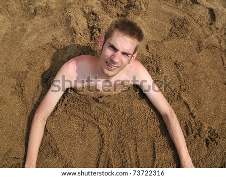 Young man buried in the sand on the beach smiling up at the camera, having fun