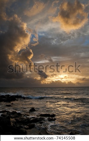 Ocean with a golden sunset shining through the Hawaii clouds