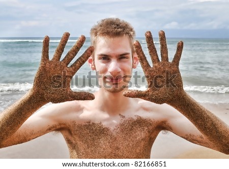 Beach fun with a young attractive male with sand all over his body. Ocean sandy beach waves in the background.