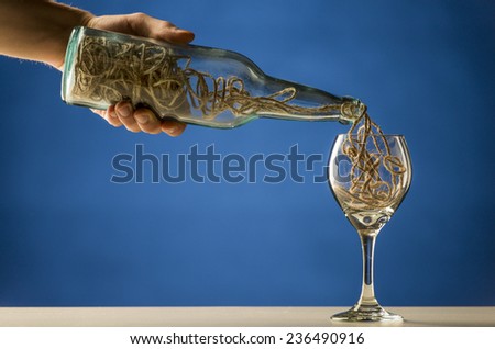 Man pouring a tangled mass of string from a transparent wine bottle into a wineglass in a conceptual image over blue with copyspace