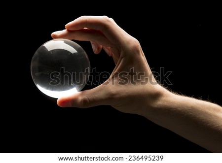 Hand holding a clear transparent crystal glass ball isolated on black background