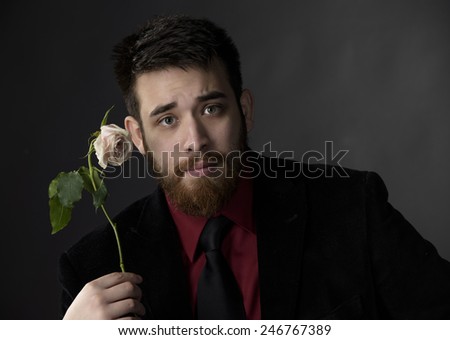 Close up Serious Handsome Young Man in Formal Attire Holding Rose Flower While Looking at the Camera. Captured on Gray Background