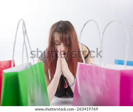 Young Woman with Red Hair Praying with Eyes Closed near Collection of Colorful Shopping Bags