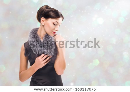 Elegant brunette winter shining background / young woman in a black silk dress and fur collar