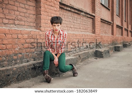 Sadness. Young woman plaid shirt jeans near brick wall. Looking into the camera.