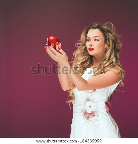 The girl with an apple. Beauty Photo of a beautiful young woman in a cocktail dress. Blonde with long wavy hair.