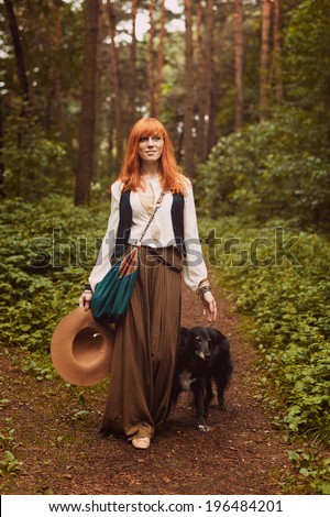 Portrait of romantic hippie woman smile in the woods. Young girl with hippie dress walking in the forest. Redhead girl in boho style.