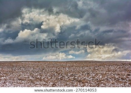 Winter rural landscape - agricultural fields and storm clouds on the sky