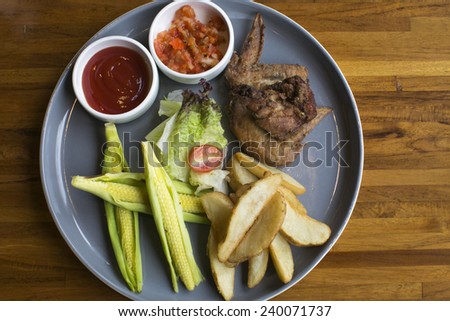 A organic food platter pus on a wood desk. Includes french fries, salad, corn, chicken, ketchup and tartar sauce. Leave the space on the right side for text.