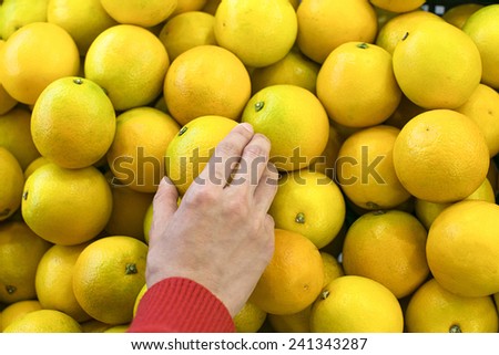 A woman\'s hand pick up an organic orange in a market. Close up with blur background.