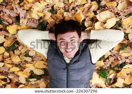Happy asian man lying on the yellow leaves in park