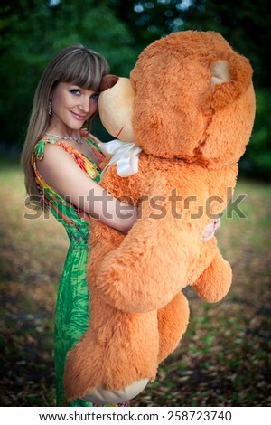 beautiful woman keeps big and orange toy teddy bear. outdoors in the park