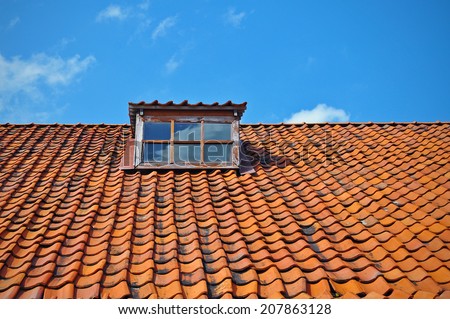 Upper part of medieval tile roof with window with a blue sky back