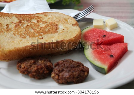 French toast with fresh red melon , fried pork and butter on white plate.
